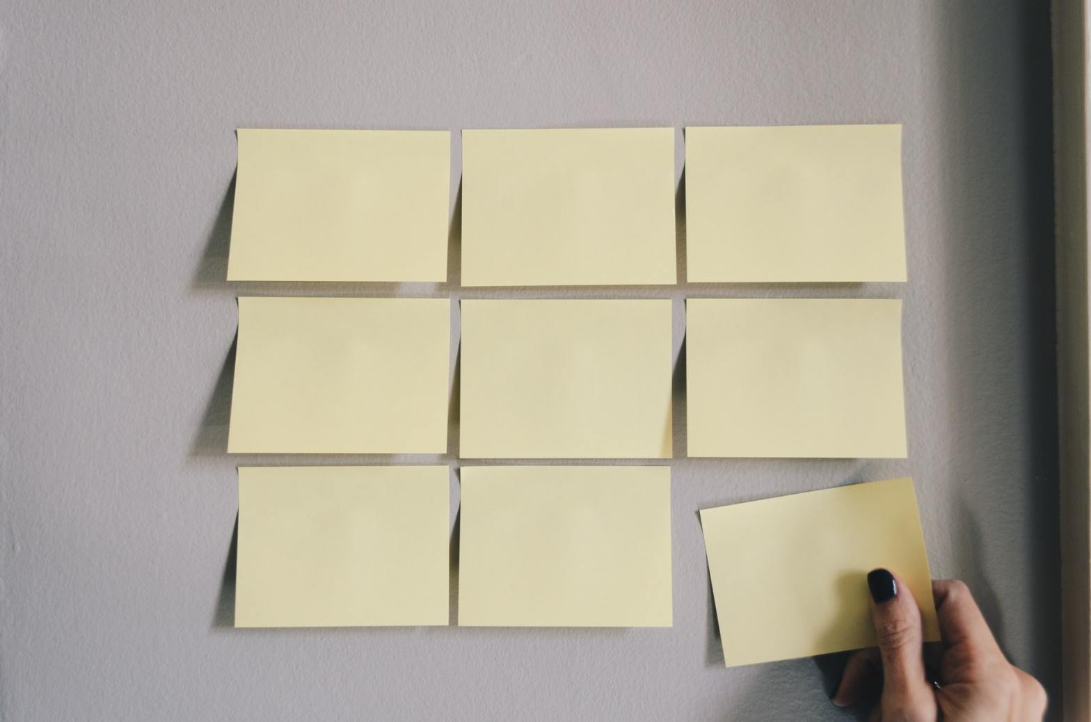 A hand placing post-it notes in a 3x3 arrangement. Photo by Kelly Sikkema on Unsplash